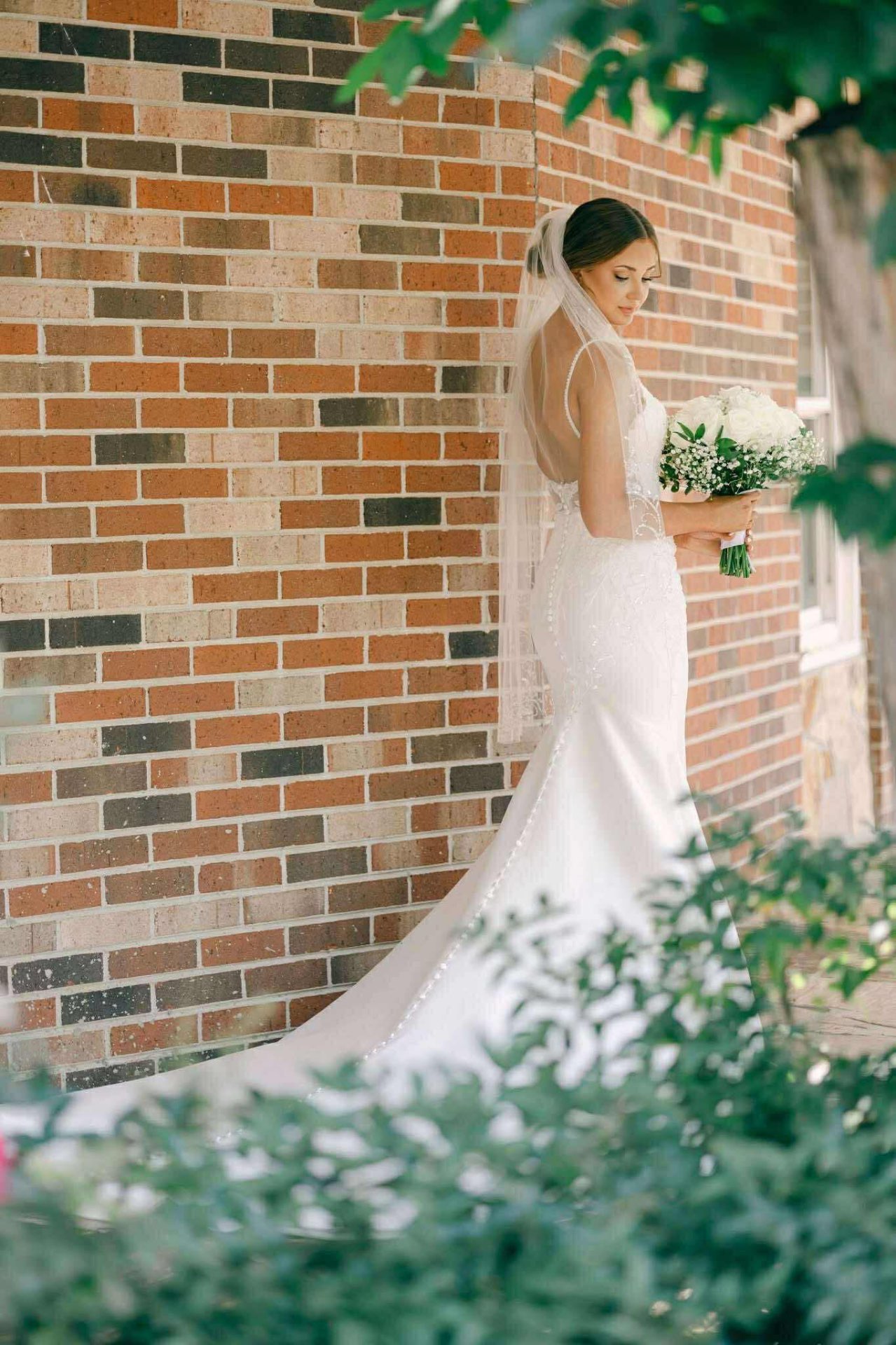Bride in fitted lace gown with cathedral veil by brick wall